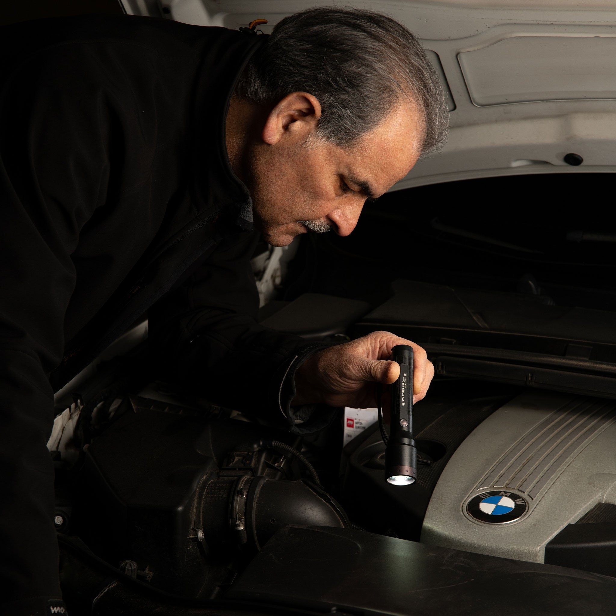 Ledlenser P6R Core Torch handheld flashlight in use under a car hood held by a man lighting the engine bay