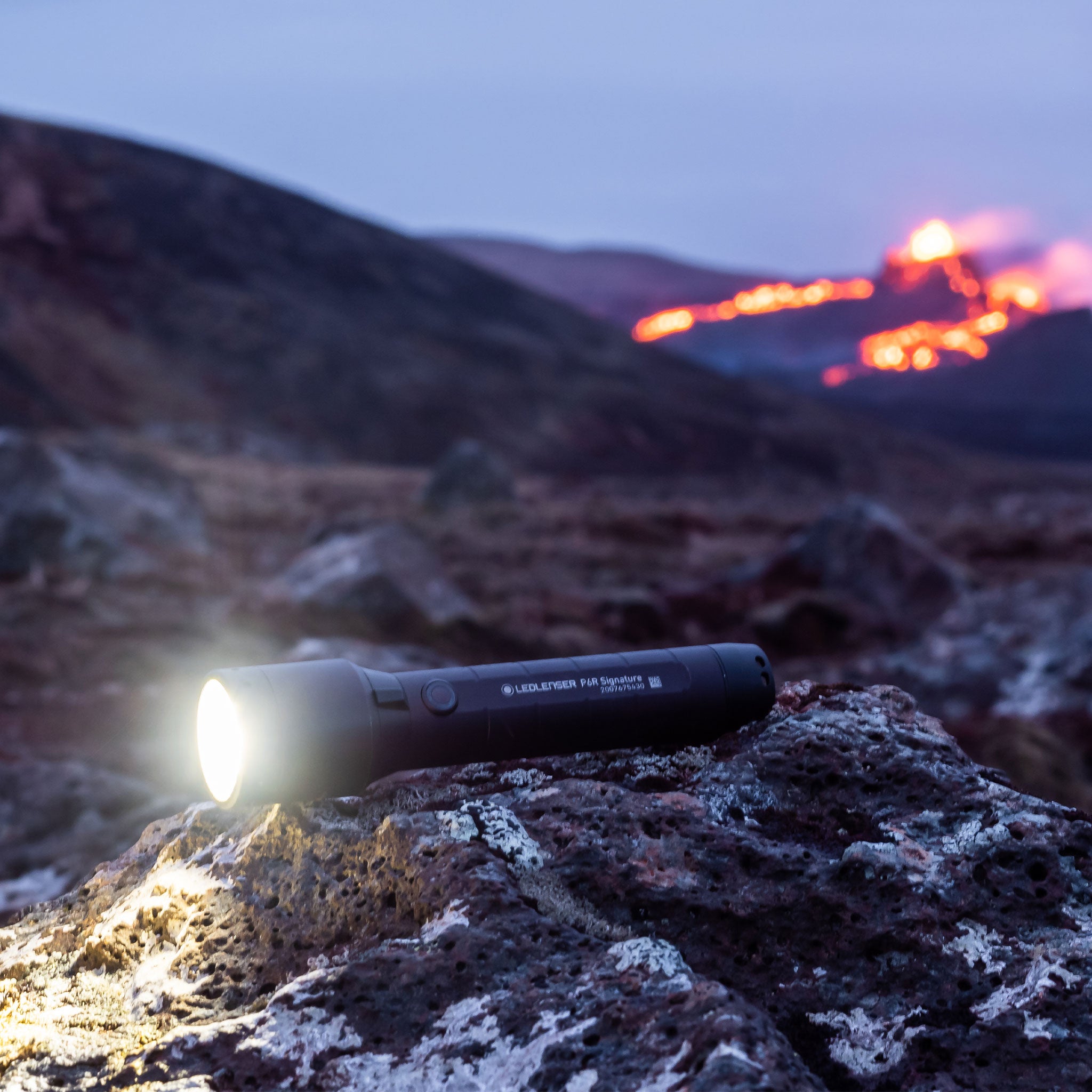 P6R Signature Torch resting on rocks outdoors with the front beam illuminated; a black cylindrical Ledlenser torch in a rugged outdoor setting
