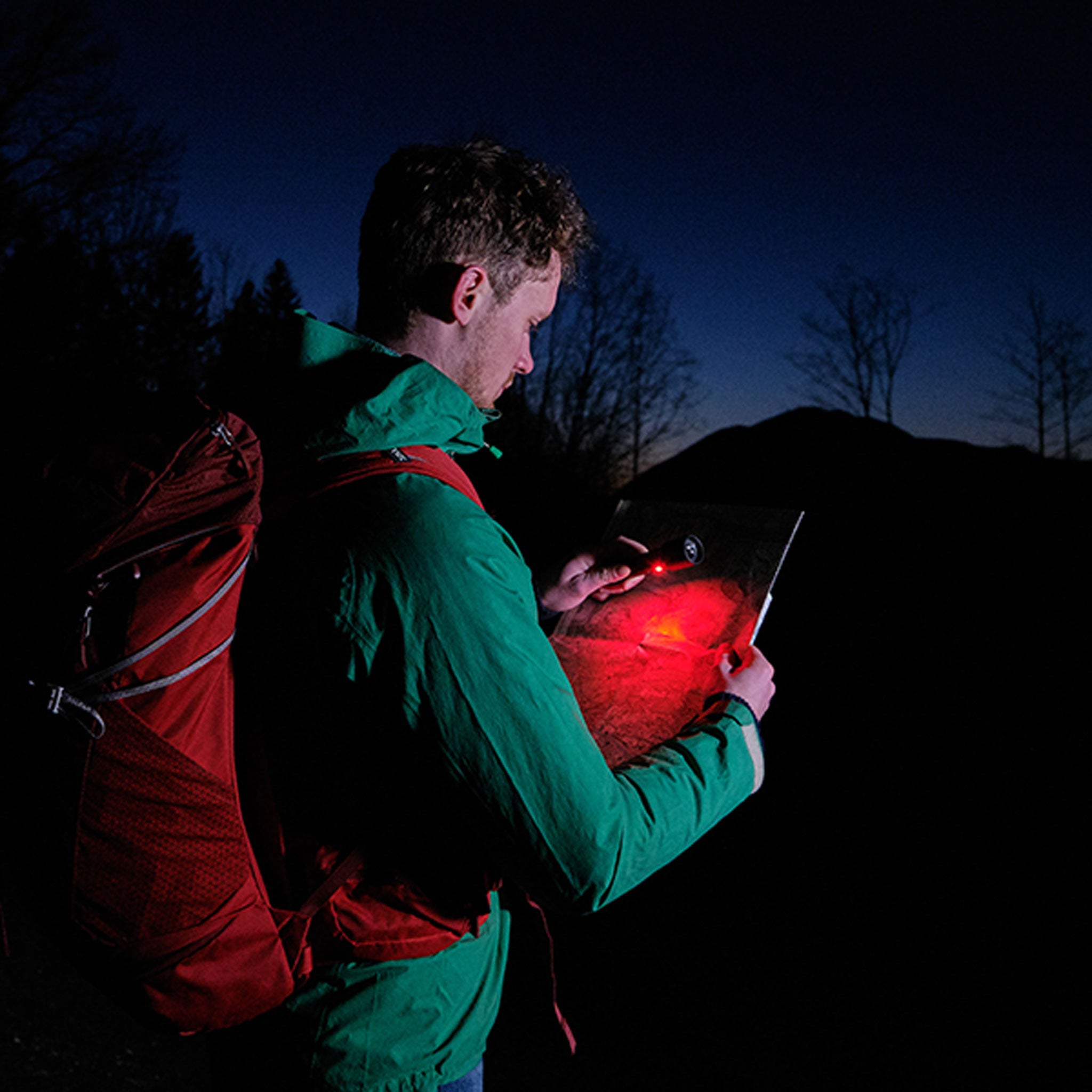 Ledlenser P6R Signature Torch in use outdoors at night; person with green jacket and red backpack holds a tablet emitting red light
