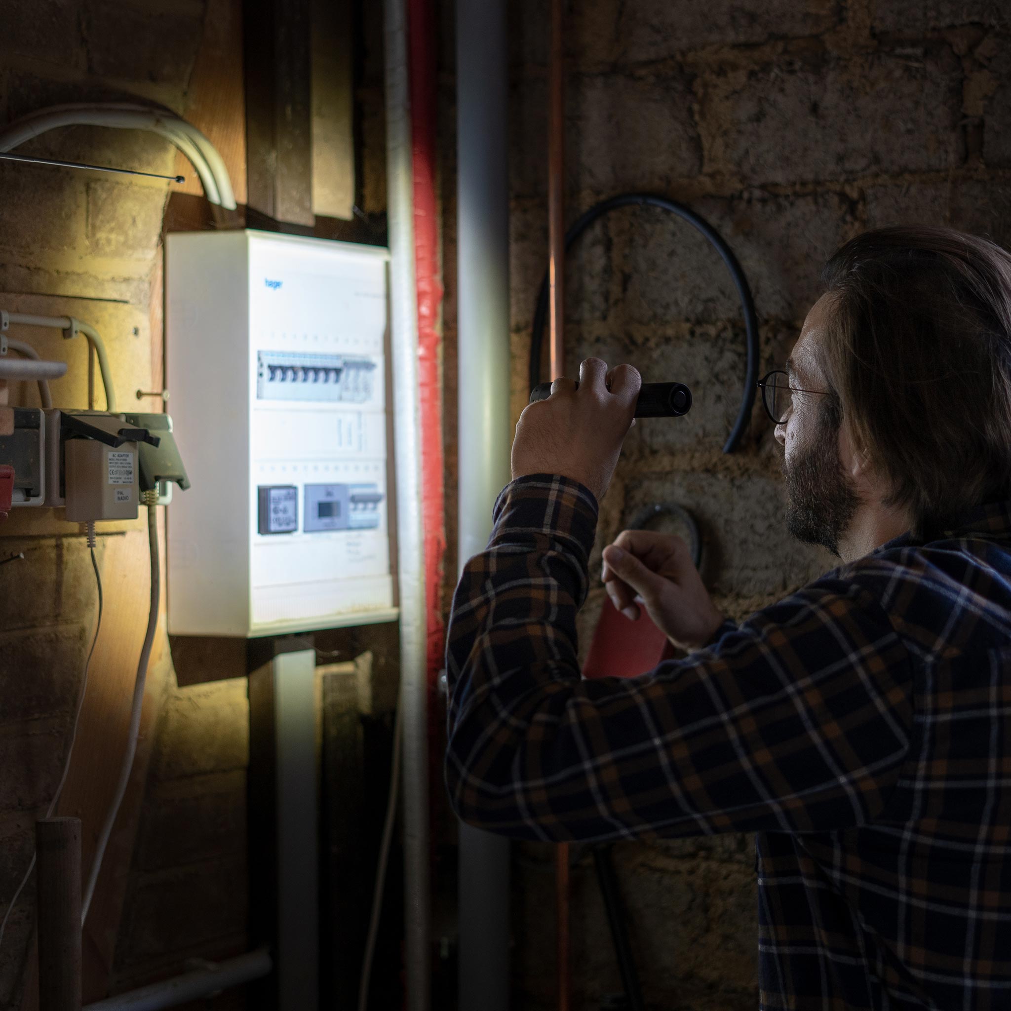 P7 Core Torch held by a man in a plaid shirt inspecting an electrical panel in a dim basement utility room