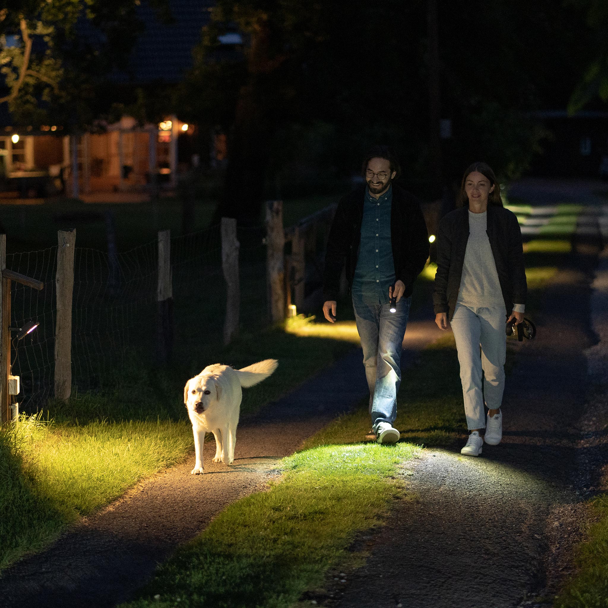 P7 Core Torch held by a man walking with a woman and a white dog on a dim nighttime path beam lighting the foreground