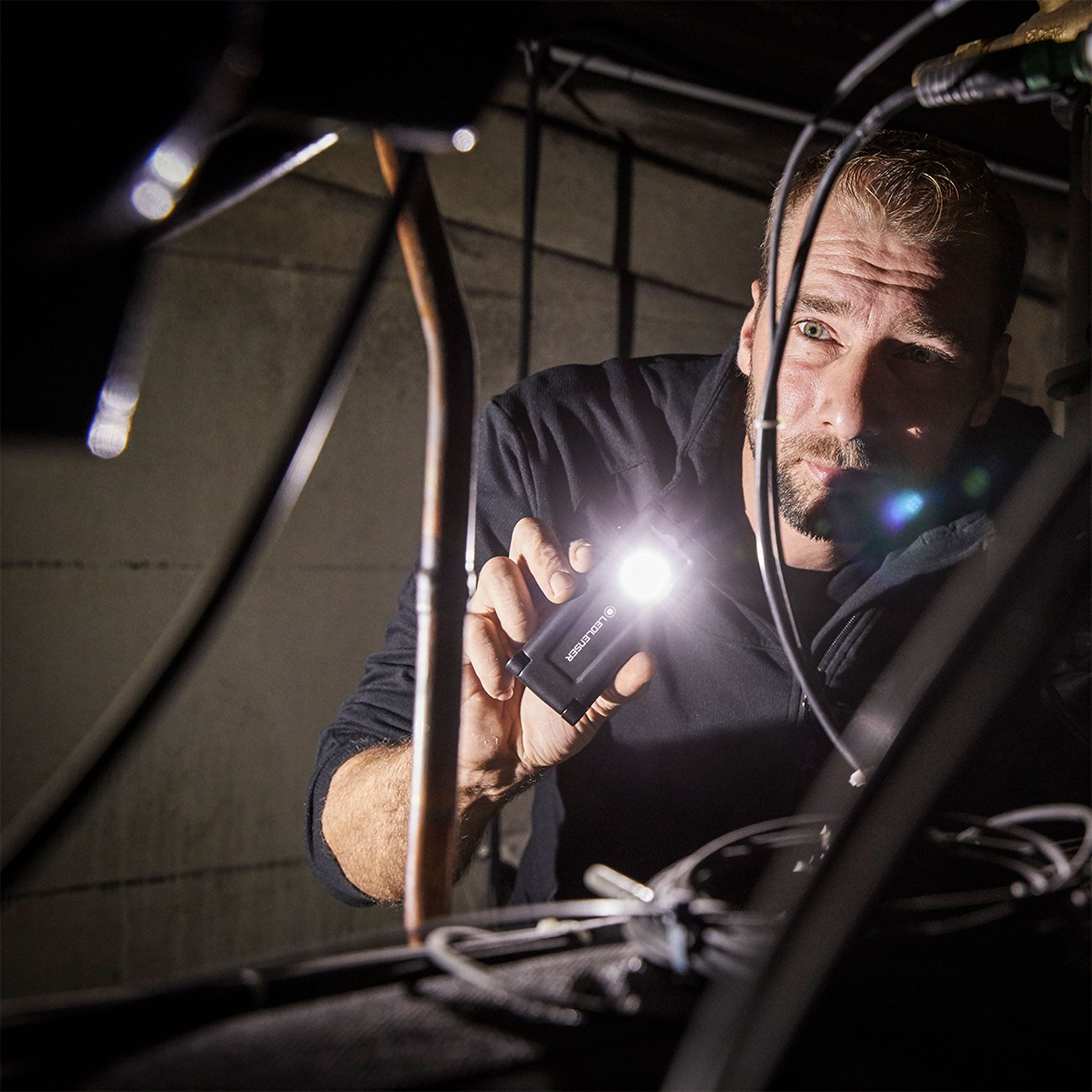 iF2R Spotlight held by a man in a dim workshop compact rechargeable Ledlenser torch with illuminated beam among cables