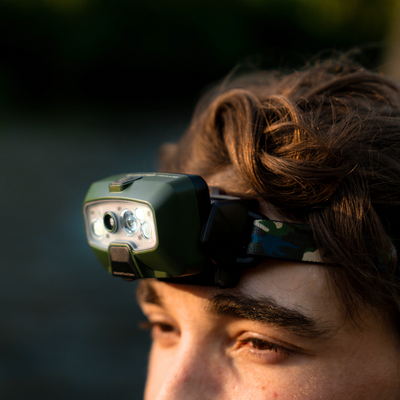 HF8R Core RGB Camo headlamp worn on a camo strap across the forehead angled side view showing green body and multiple LEDs