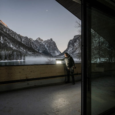 Ledlenser AF12R Work Floodlight mounted on a balcony railing with a person nearby and snowy mountains in the background