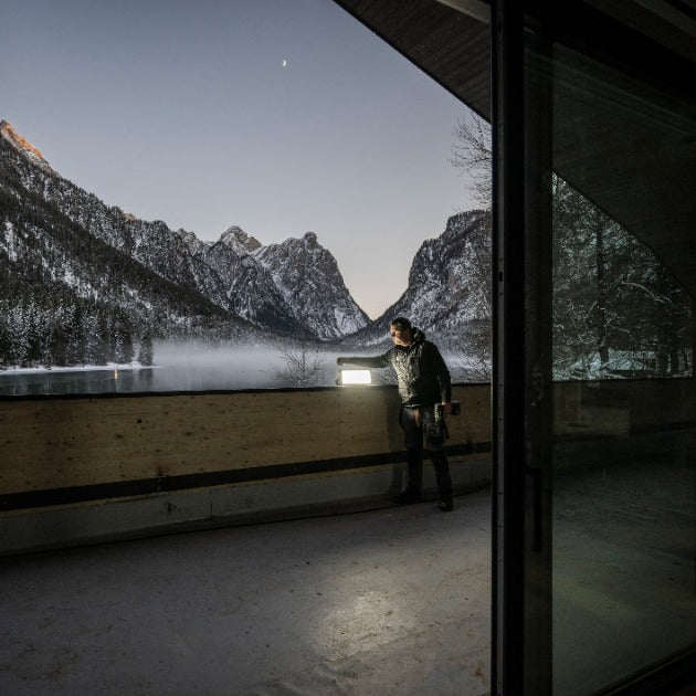 Ledlenser AF12R Work Floodlight mounted on a balcony railing with a person nearby and snowy mountains in the background