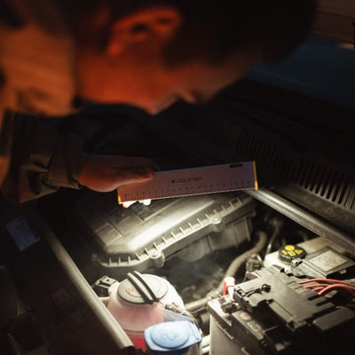 AF2R Work Area Light held by hand in a dark engine bay illuminating automotive components