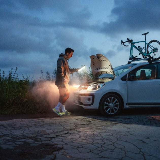 Ledlenser AF2R Work Area Light held by a person beside a car with a bicycle on the roof rack at dusk