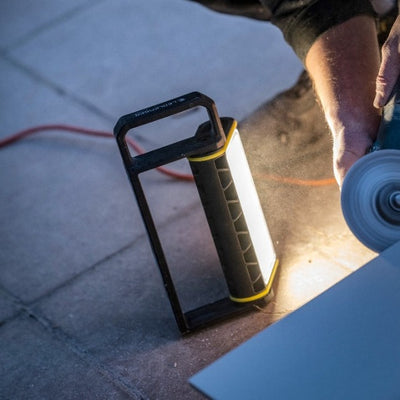 AF4R Work Floodlight with black handle frame and yellow accents standing on the floor beside a rotating grinding wheel