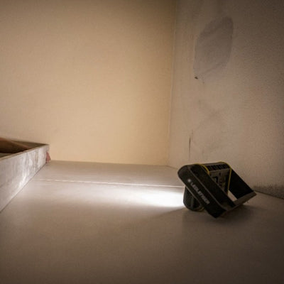 AF4R Work Floodlight by Ledlenser tilted on a white surface emitting a focused beam in a dim indoor space