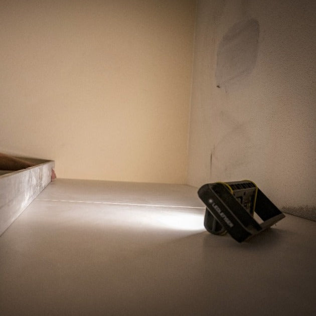 AF4R Work Floodlight by Ledlenser tilted on a white surface emitting a focused beam in a dim indoor space