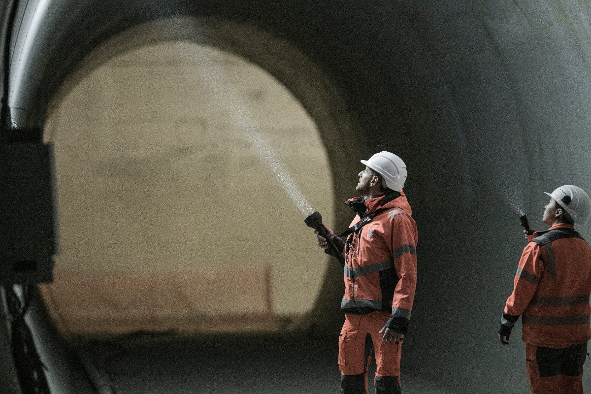 P21R Torch in use by two workers in orange safety gear and helmets inside a tunnel beam of light visible