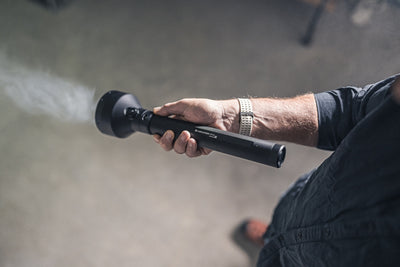 Ledlenser P21R Torch held in a right hand black textured flashlight with a prominent head worn with a dark shirt and beige watch