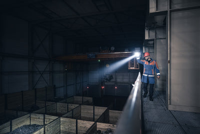 Ledlenser P21R Torch held by a worker in a dim industrial facility beam lighting a platform edge