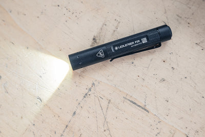 Ledlenser P2R Torch compact black flashlight on a light wood surface with its beam visible