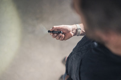 P2R Torch held in a right hand pointing forward small black rechargeable torch with a beam visible in outdoor setting; wearer has a silver wristwatch