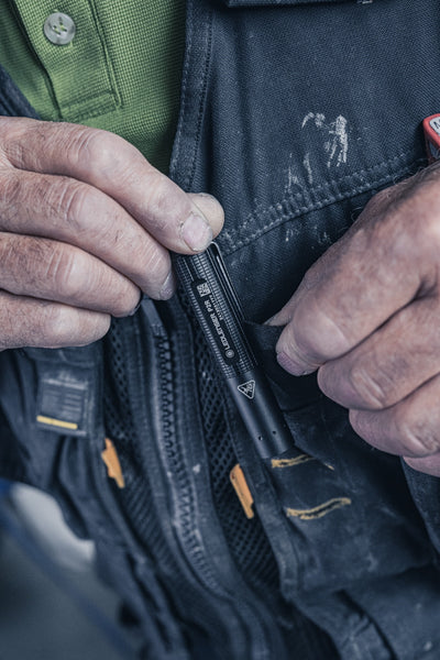 P2R Torch by Ledlenser a compact black rechargeable torch being tucked into a tool vest pocket by a worker wearing a green shirt and dark jacket