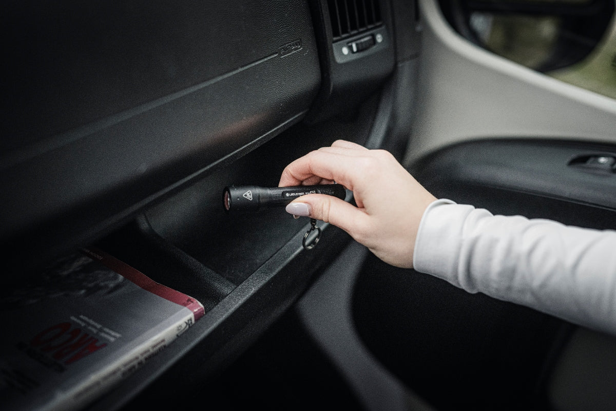P3R Torch handheld black flashlight being inserted into a car dashboard compartment by a user