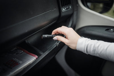 P3R Torch handheld black flashlight being inserted into a car dashboard compartment by a user