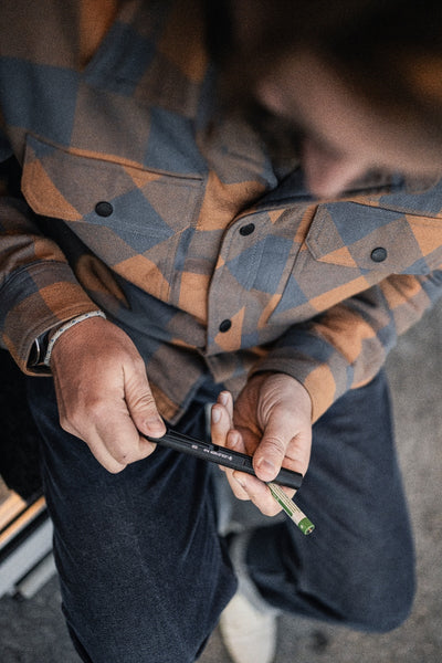 P4R Torch held in hands black pen style flashlight with green tip worn with a blue orange plaid shirt