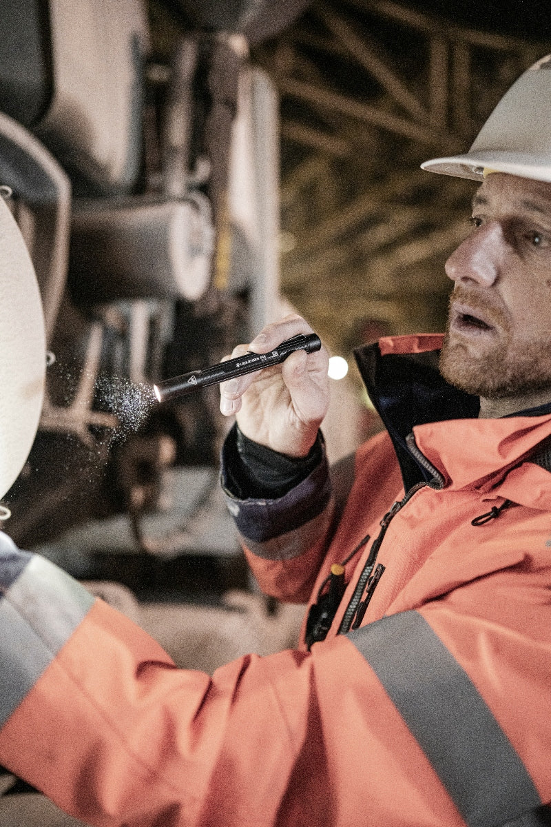 Ledlenser P4R Torch held by a worker in orange safety jacket and white hard hat in an industrial workshop environment