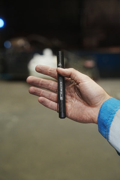 Ledlenser P4R Torch held in a hand compact black pen style torch with a visible clip against a dim background