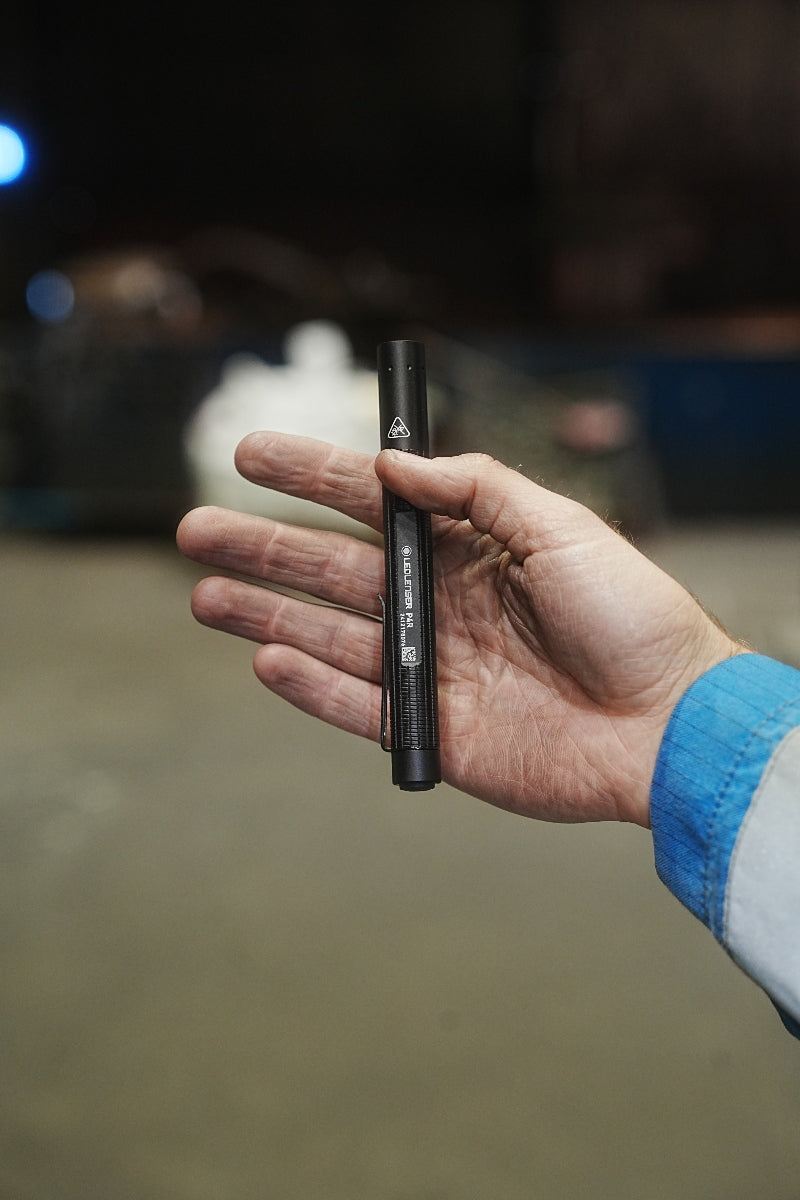 Ledlenser P4R Torch held in a hand compact black pen style torch with a visible clip against a dim background