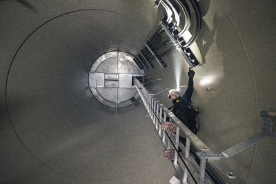 Ledlenser P5R Pro Torch used by a worker in helmet inside an industrial vertical shaft standing on a metal ladder and reaching with a handheld light