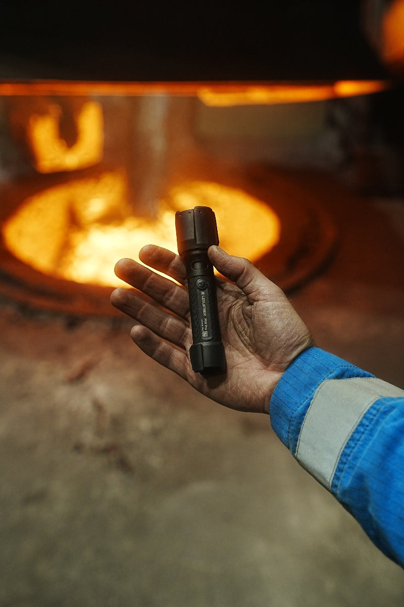 Ledlenser P5R Pro Torch held in a gloved hand black compact rechargeable torch with textured grip in front of a molten metal furnace