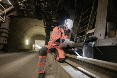 P5R Pro Torch in a tunnel a worker in orange safety gear and white helmet using a tablet with a headlamp illuminated