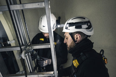 P5R Torch mounted on a white safety helmet worn by a worker in an industrial ladder setting with another worker in the background