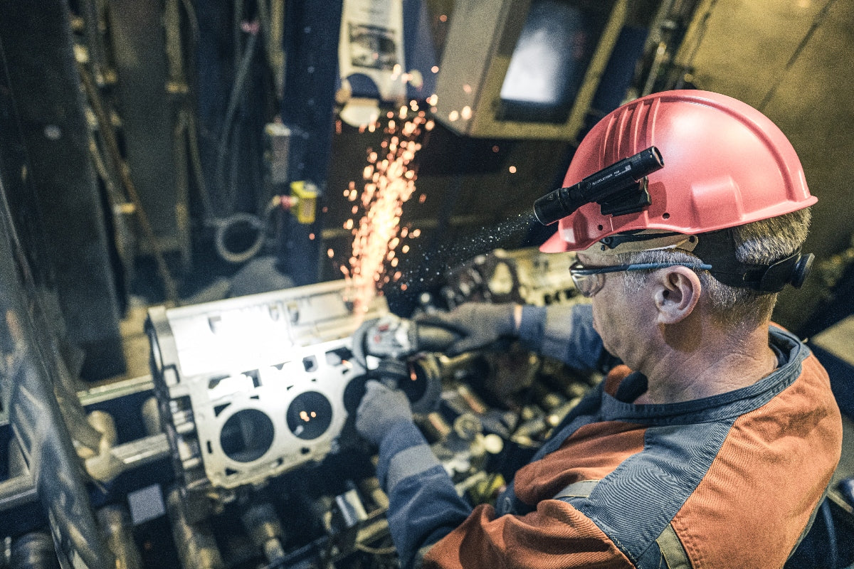 P5R Torch mounted on a pink safety helmet worn by a worker welding in an industrial workshop with sparks flying