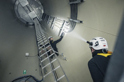 P5R Torch being used inside an industrial shaft with a worker on a ladder wearing a helmet and headlamp projecting light toward the wall