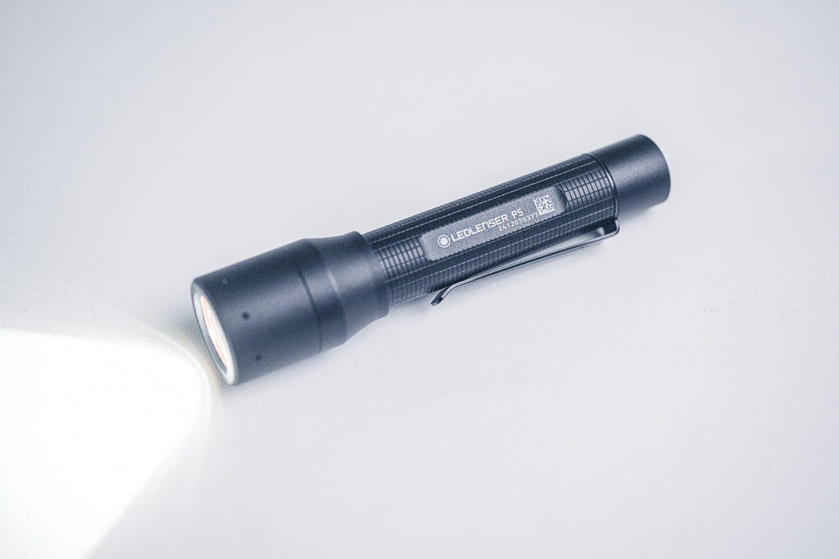Ledlenser P5 Torch lying on a white surface with a beam of light projecting to the left