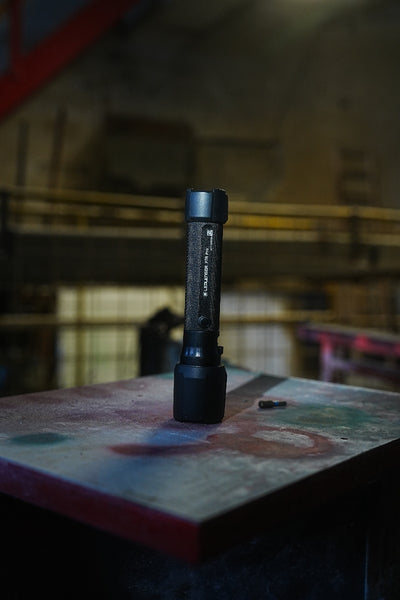 Ledlenser P7R Pro Torch standing upright on a dusty workshop worktable in a dim industrial setting