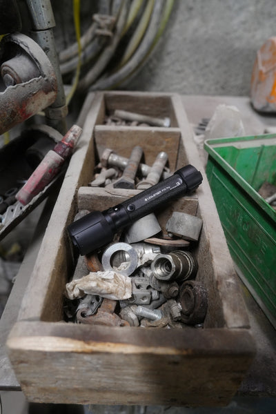 Ledlenser P7R Pro Torch resting in a wooden tool tray among nuts bolts and metal parts in a workshop environment