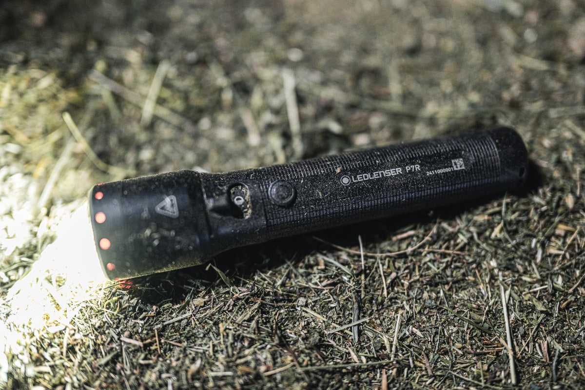 Ledlenser P7R Torch resting on grass at night with light on black compact rechargeable flashlight