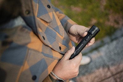 Ledlenser P7R Torch held in hands outdoors black compact rechargeable flashlight with textured grip plaid jacket in background