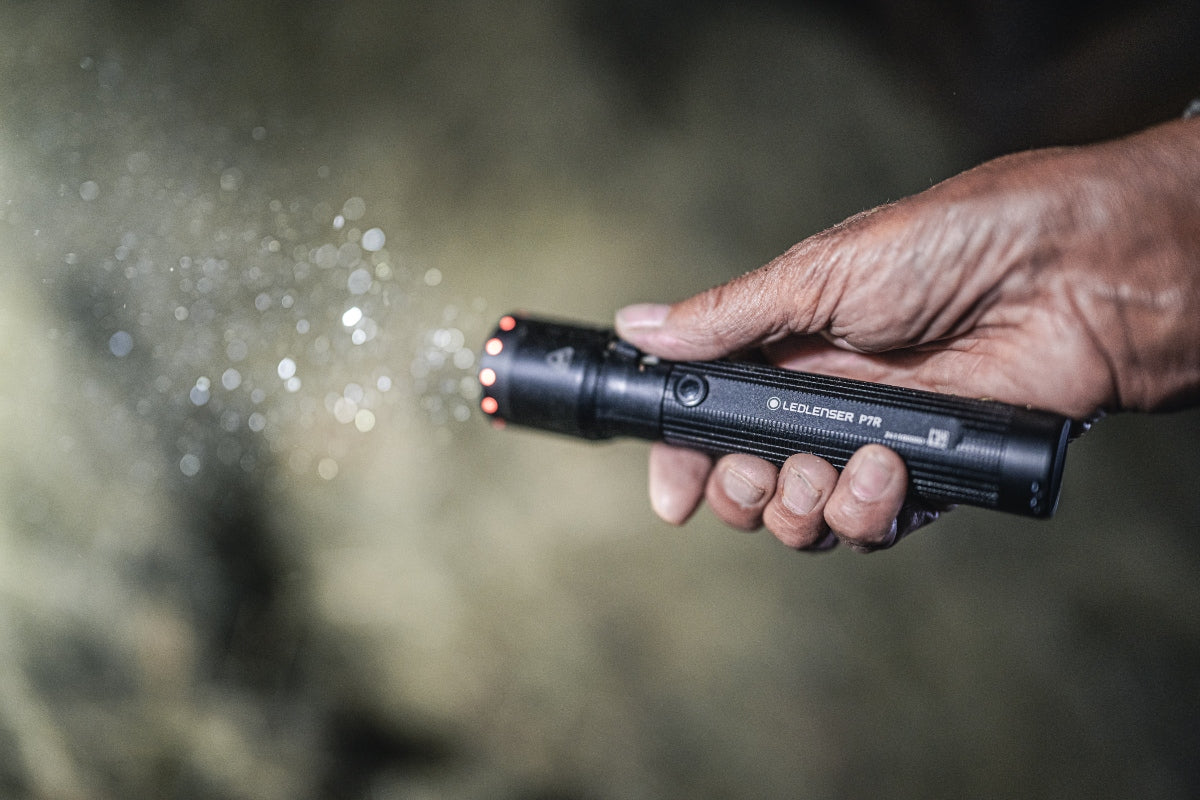 Ledlenser P7R torch held in a dark hand black cylindrical flashlight with a red LED ring at the head and textured grip