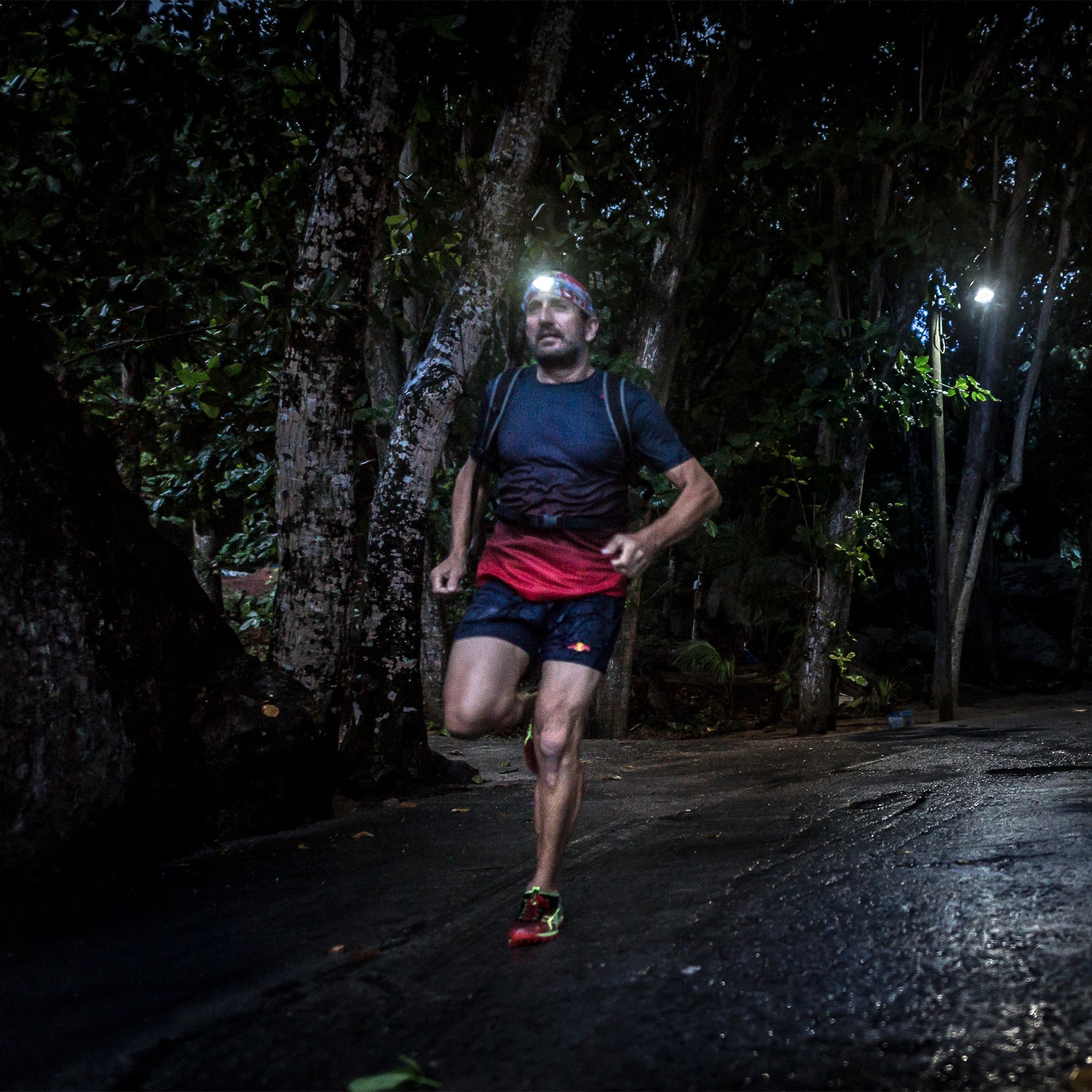 NEO Blue Battery Operated Headlamp worn by a runner at night in a forest with the headlamp on