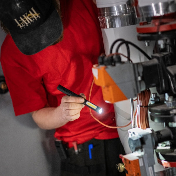 Technician in red shirt using a handheld W2R Work Pen and Test Light to illuminate a piece of industrial equipment