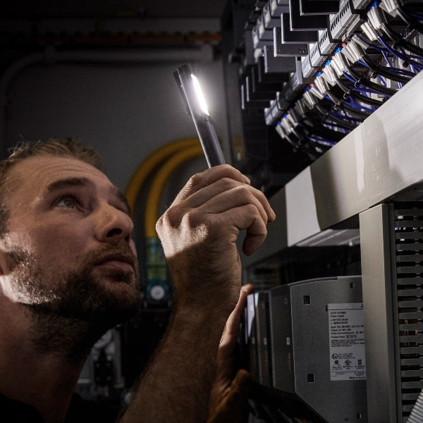 Ledlenser W2R Work Pen and Test Light held by a technician inspecting equipment rack in a server room