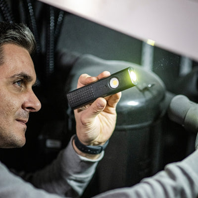Ledlenser W5R Work Light held by a man in a dim workshop a compact black handheld light with front LED illuminated