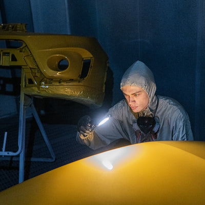 W7R Work Light being used by a technician in a dim workshop handheld light illuminating a yellow vehicle panel