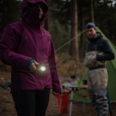 P7R Signature Torch held by a person in a purple jacket at a campsite with the torch emitting a bright beam