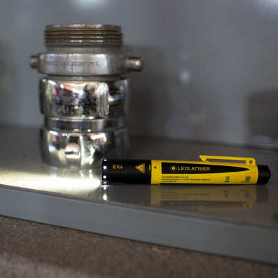 EX4 Torch by Ledlenser yellow and black handheld flashlight lying on a reflective surface with a metallic valve fitting in the background
