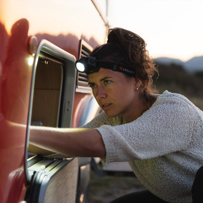 H15R Core Headlamp worn on headband by a person leaning toward an open car door at dusk with the light on