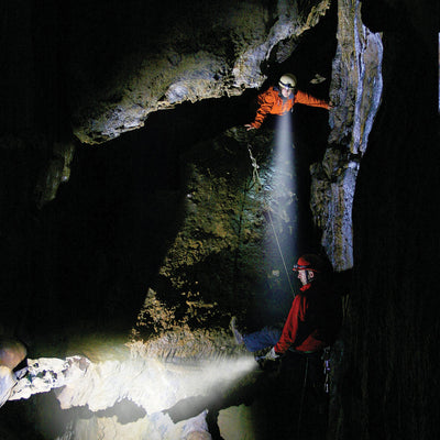 Ledlenser H3 2 Battery Operated Headlamp in use by two cavers in a dark cave orange and red jackets with a bright beam emerging from the headlamp
