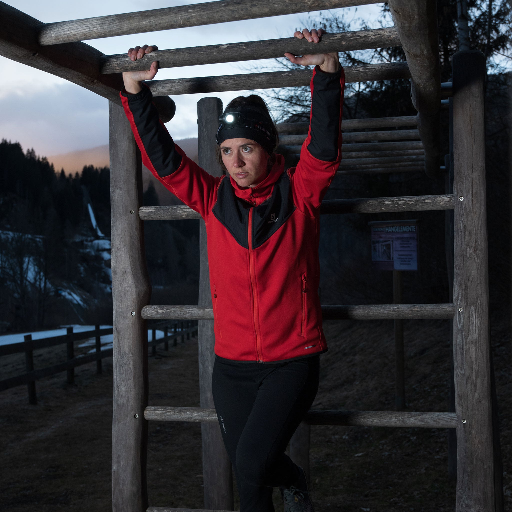 Ledlenser H5 Core Headlamp worn by a person in a red and black jacket on a wooden outdoor climbing frame headlamp lit