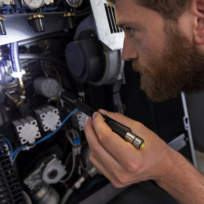 Technician holding a Ledlenser i6R Rechargeable Pen Light beside industrial machinery with gauges and wiring