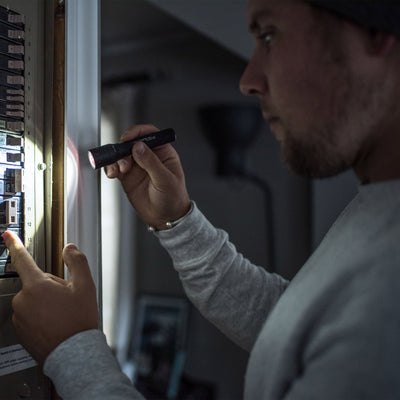 Ledlenser P5R Torch held by a person inspecting an electrical panel beam illuminating circuit breakers in a dim setting
